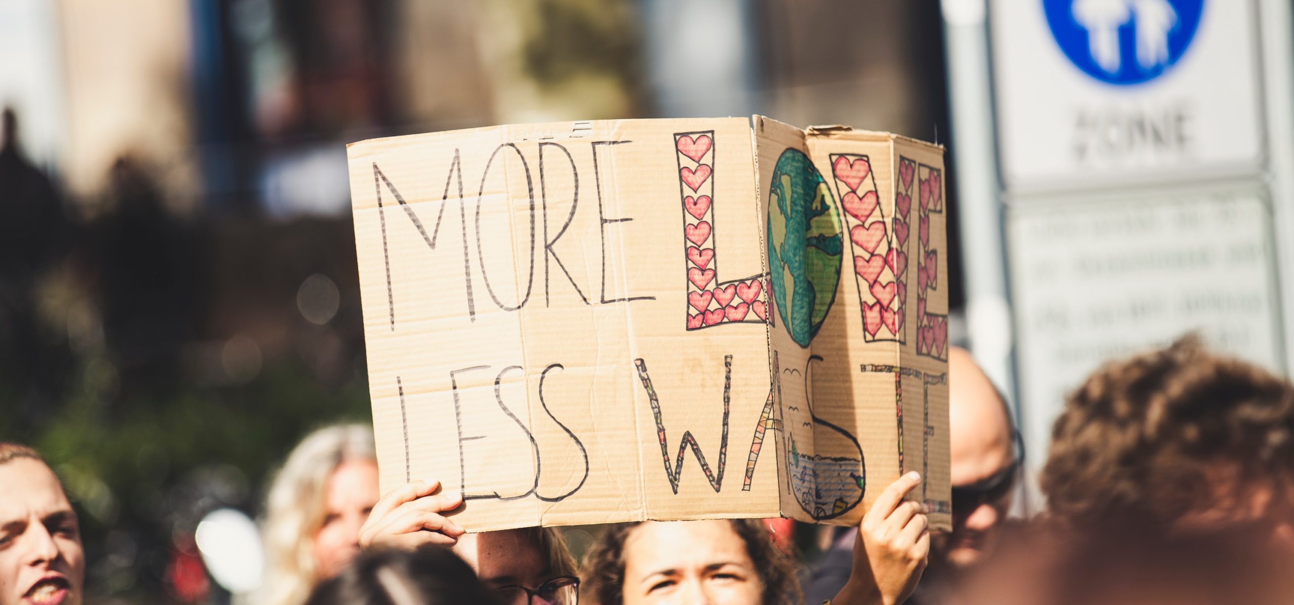 En person håller upp en demonstrationskylt med texten More Love Less Waste